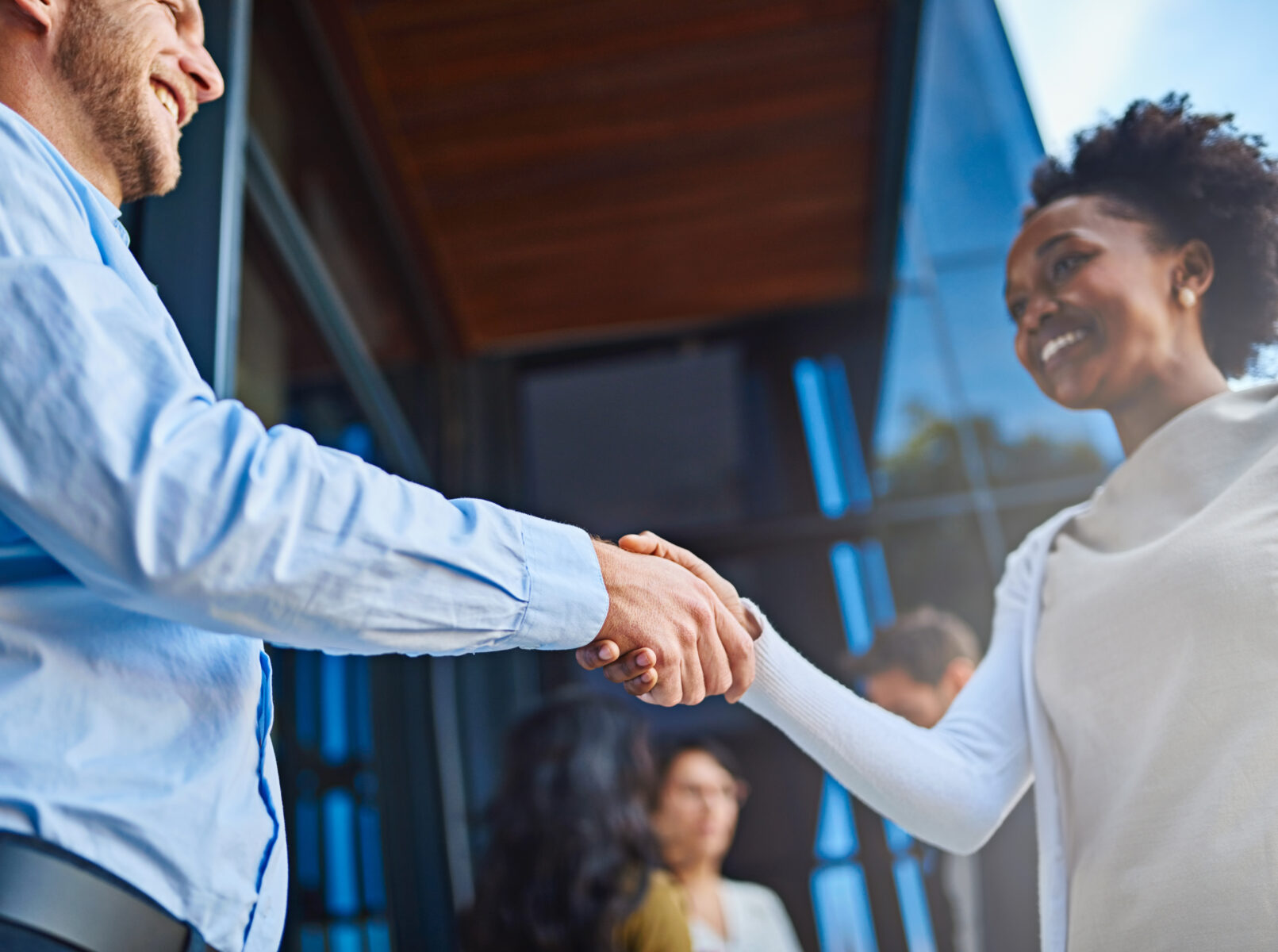 Cropped shot of two businesspeople shaking hands with their coworkers in the background.