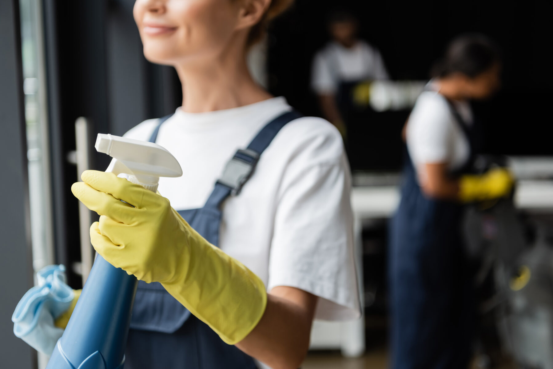 partial view of smiling woman in rubber glove holding spray bottle with detergent
