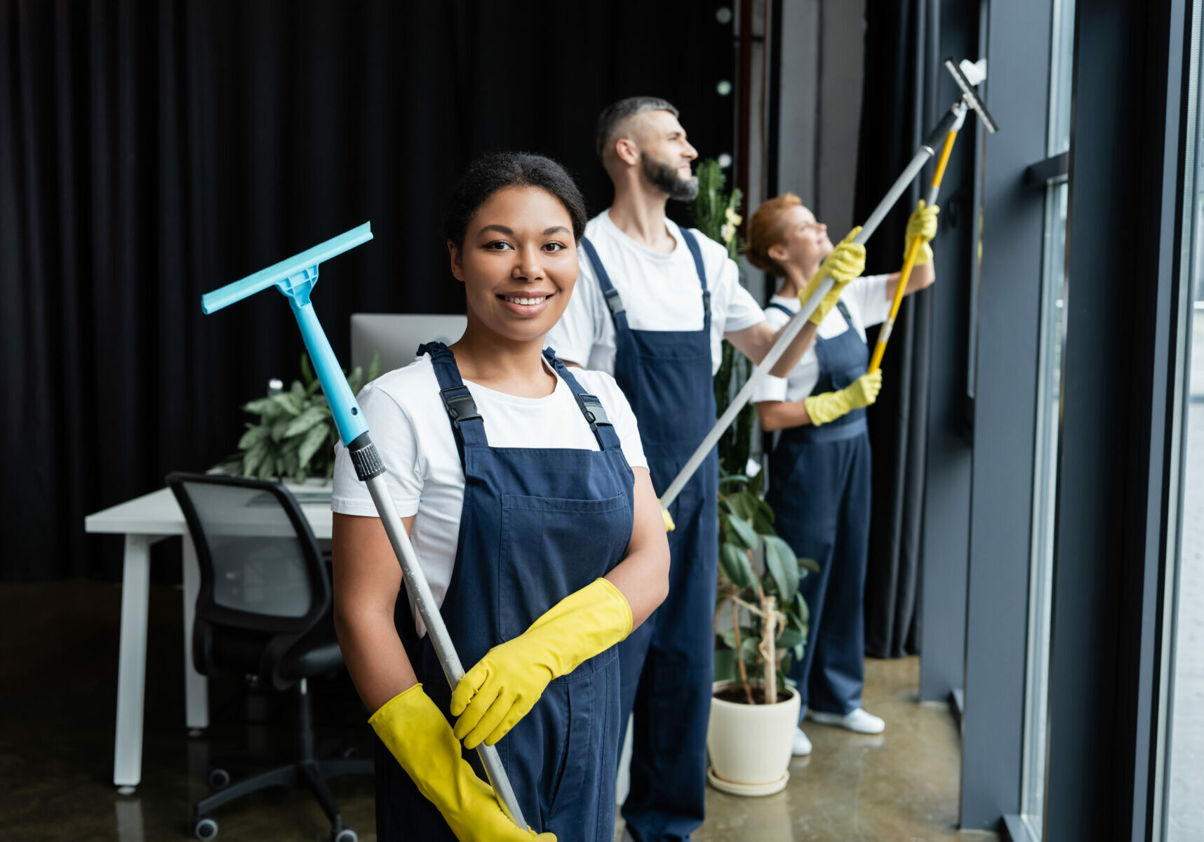 cheerful mixed race woman holding window wiper near colleagues working in office