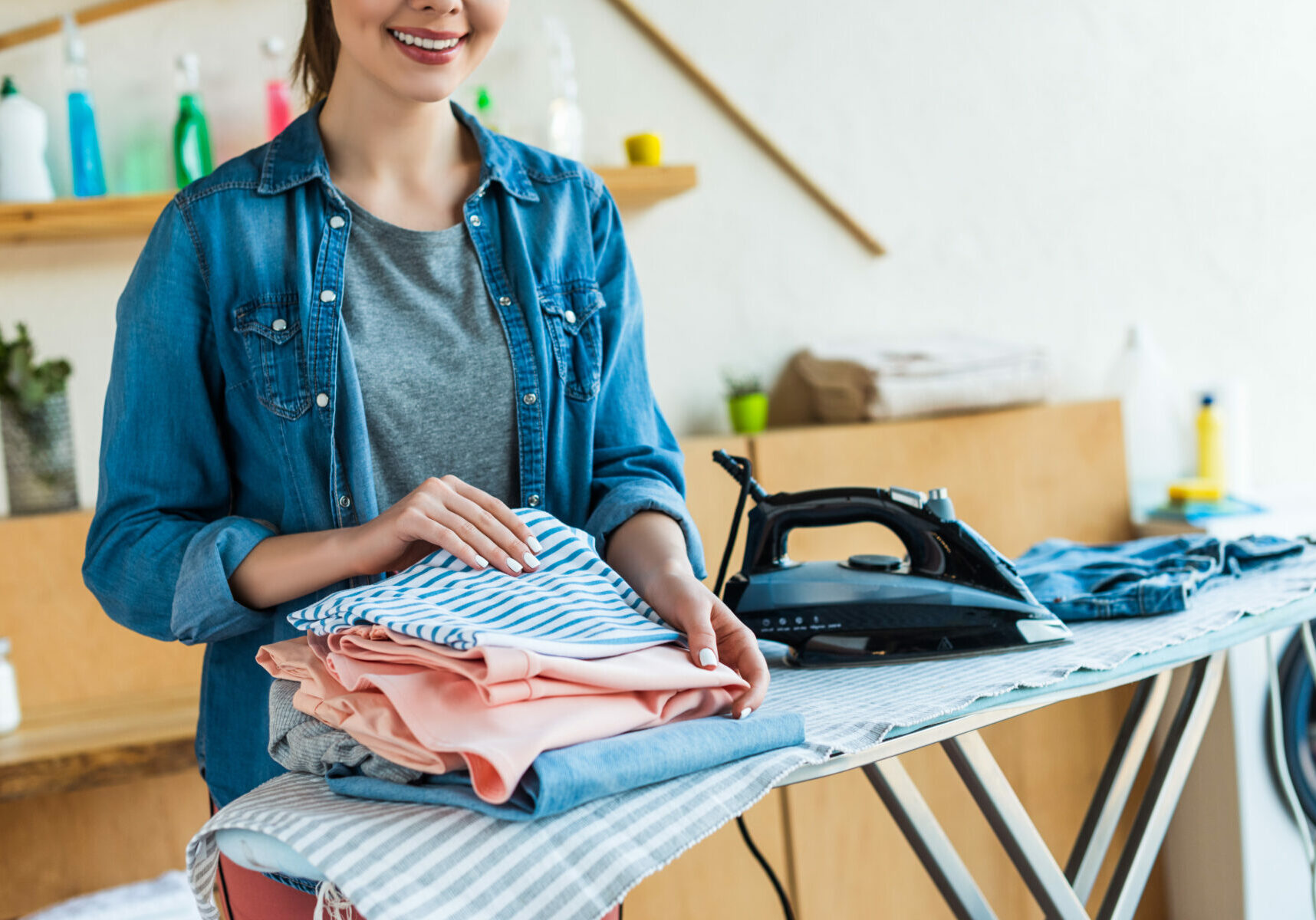 cropped shot of smiling young woman stacking clothes after ironing at home