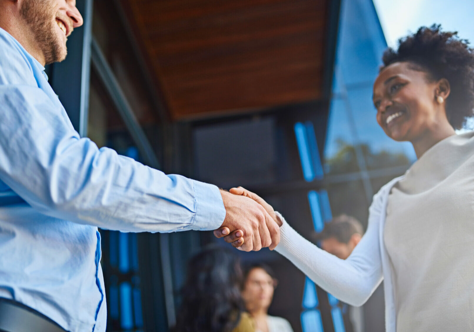 Cropped shot of two businesspeople shaking hands with their coworkers in the background.
