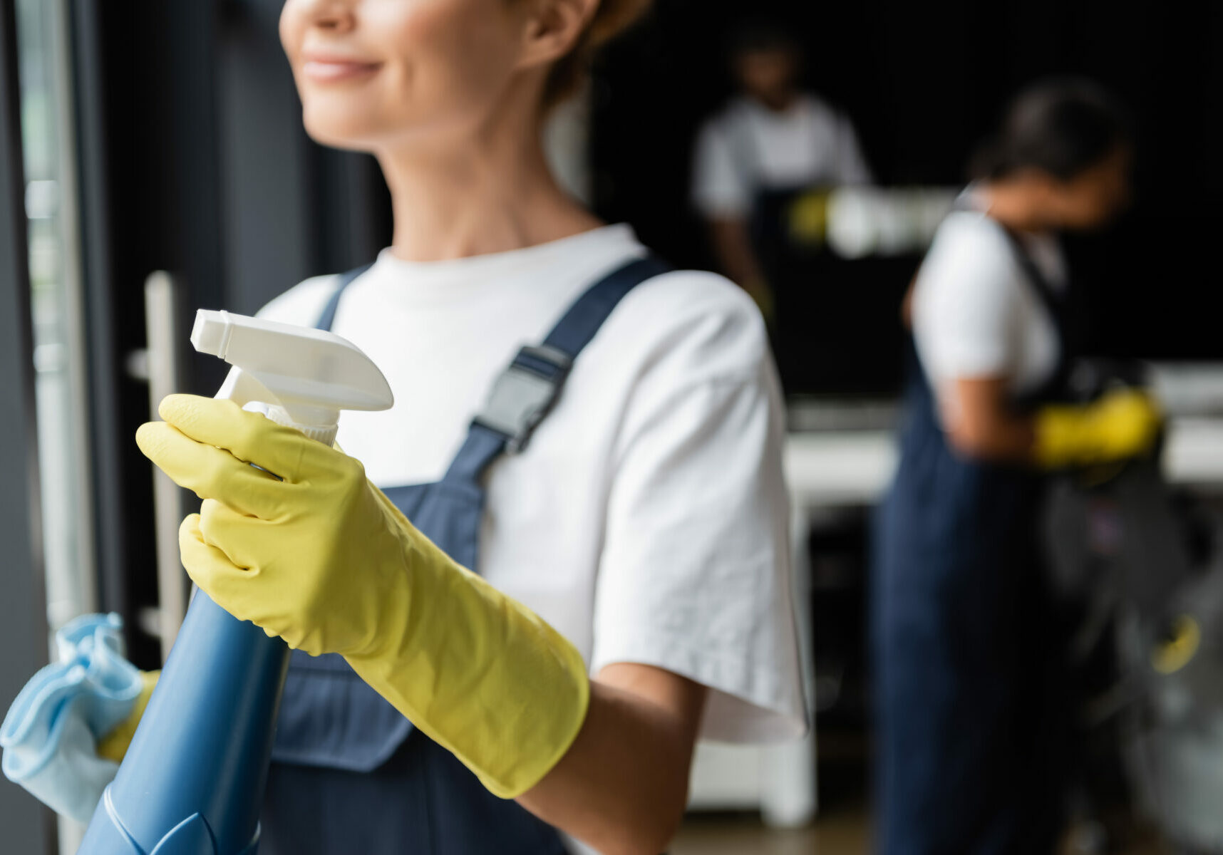 partial view of smiling woman in rubber glove holding spray bottle with detergent