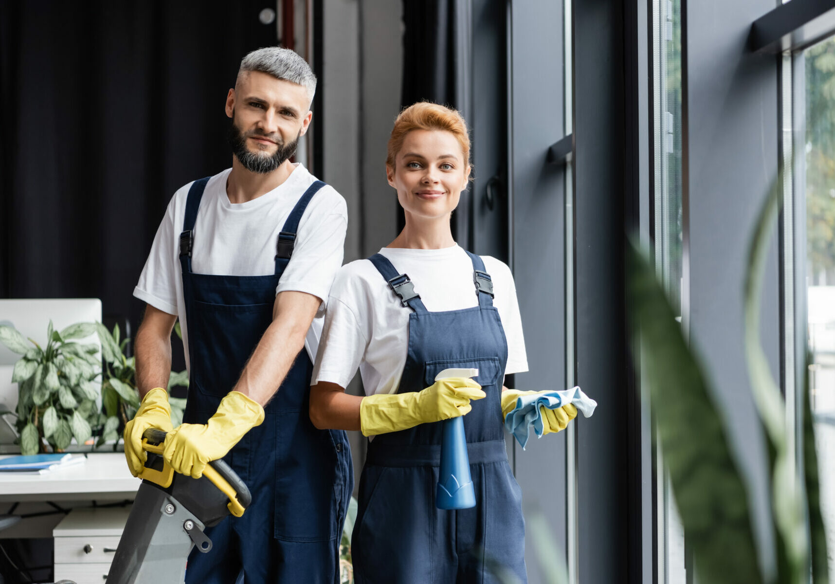 smiling professional cleaners in uniform looking at camera in office